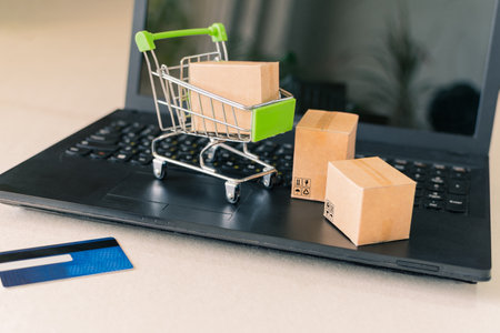 A selective focus shot of a toy pushcart and small boxes on top of a laptop for online businessの写真素材