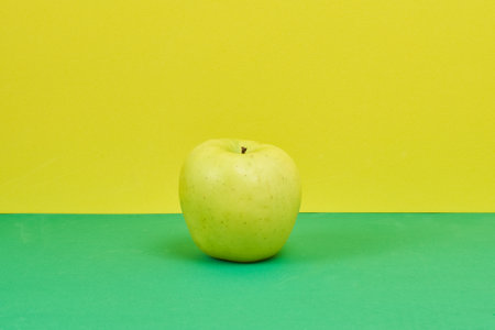 A closeup shot of an apple on a green and yellow backgroundの写真素材
