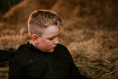 A blonde child wearing a black jacket and sitting on haycock in autumnの写真素材