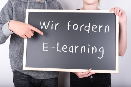 Two people holding a blackboard with 'we demand e-learning' in German written on it
