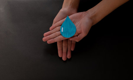 An overhead of a paper cutout of a drop of water on a woman's palm - concept of environmental...