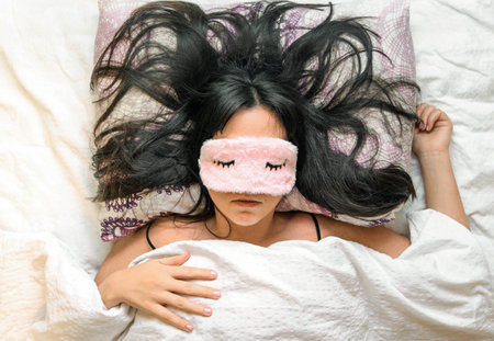 A shallow focus closeup of a female wearing a sleeping eye cover while lying on the bedの写真素材
