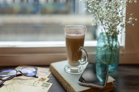 A selective focus shot of a tall glass cup with a cappuccino in front of a windowの写真素材