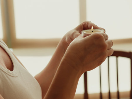 A closeup shot of female hands holding a small burning candleの写真素材