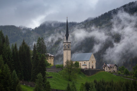 The beautiful buildings in a foggy green forest with dense trees and mountains in Dolomites, Italyの写真素材