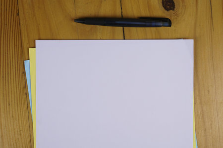A pen and colorful sheets of paper on a wooden table