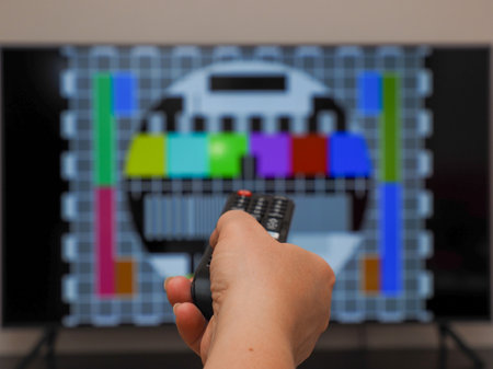 Remote control in a hand against a TV with a test screen