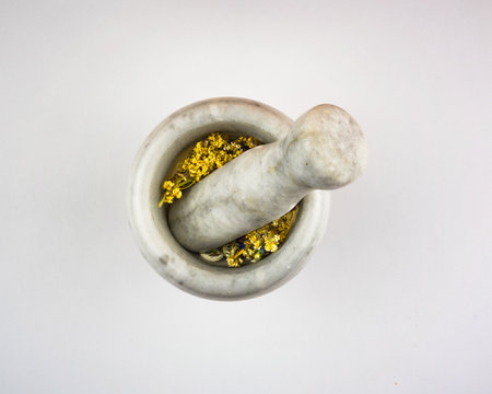 A white granite mortar with dried herbs inside