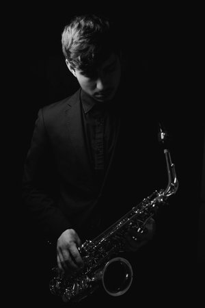 A grayscale shot of a cool and handsome guy holding his saxophone on a dark backgroundの写真素材