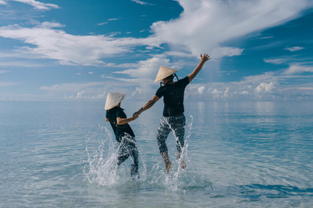A happy couple wearing hats jumping in the waterの写真素材