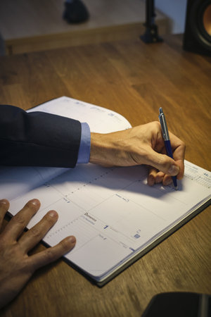 A closeup of a man's hand filling a daily planner - to-do listの写真素材