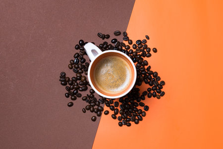 A top view of a fresh espresso cup surrounded by coffee beans on orange and brown split backgroundの写真素材
