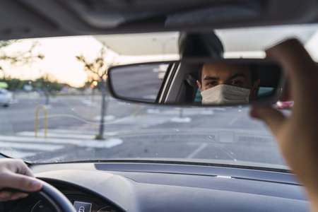 A young Caucasian male driving a car with a medical face mask - the new normal after Covid-19の写真素材