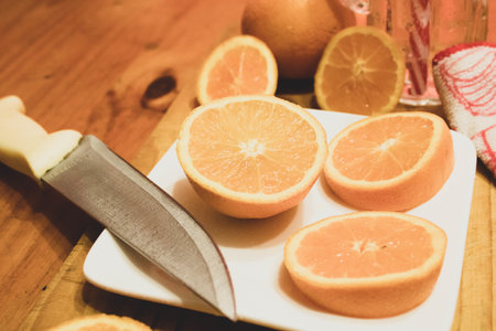 A closeup of a white plate with round cut oranges and a knife on a wooden table