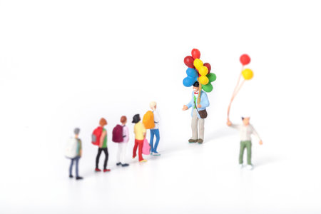A closeup shot of miniature figurines of students approaching a man holding balloonsの写真素材