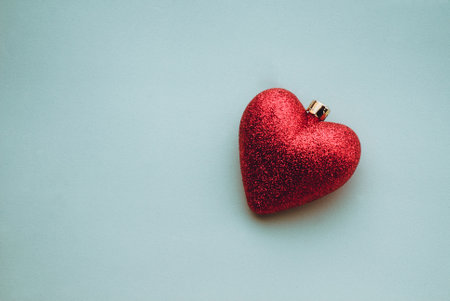 A closeup shot of shiny heart-shaped Christmas tree decoration on a light blue backgroundの写真素材