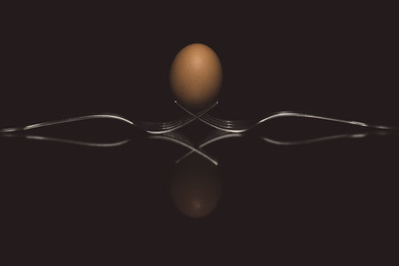 An abstract shot of two forks holding an egg on a reflecting surface