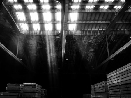 A grayscale shot of an old wooden building with the sun rays breaking through the broken roofの写真素材