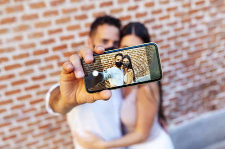 A sweet Caucasian couple taking a selfie while wearing facemask with a blurred backgroundの写真素材