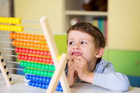 A cute Caucasian toddler boy having difficulties using the abacusの写真素材
