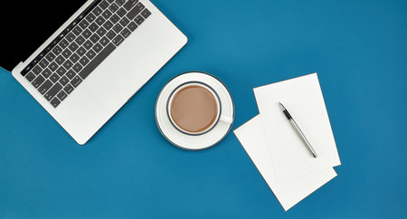 A top view of a cup of coffee, laptop, papers, and a pen on a blue surface