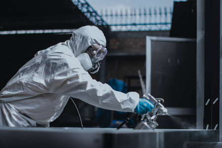 A person in protective coverall suit, goggles, and gas protection mask spray painting in a workshop