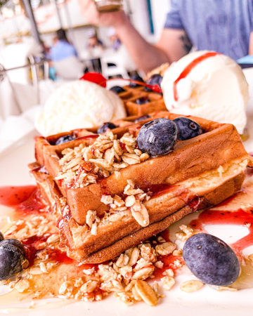 A closeup of Belgian waffles and ice cream with jam, berries, and nuts on a plateの写真素材