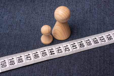 A top view of the soft tailor tape measure on a jeans material with small wooden figurines