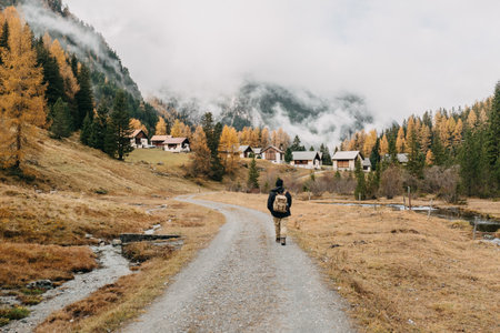 A back view of a male hiker with a backpack walking along a footpath surrounded by autumn nature scenesの写真素材