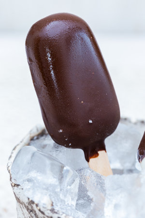 A vertical closeup shot of vegan ice-cream on sticks in a bowl with ice cubes on a tableの写真素材