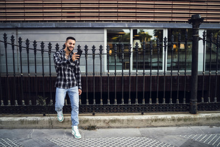 A young male with a beard wearing a black flannel shirt and video calling on the streetの写真素材