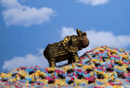 Statue of a Hindu elephant for good luck with some gems and a banknote climbing a mountain of colored cloth and a sky background with cloudsの写真素材