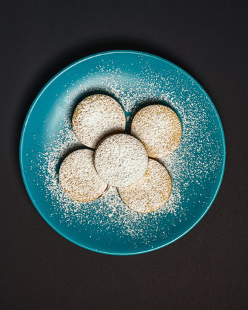A vertical shot of the top view of cookies covered in powdered sugar on a blue plateの写真素材