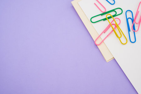 A closeup shot of a blank paper with colorful paper clips on a purple backgroundの写真素材