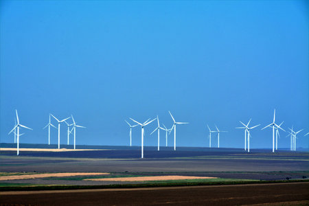 A horizontal shot of wind turbines in the countryside, cloudless sky in the background