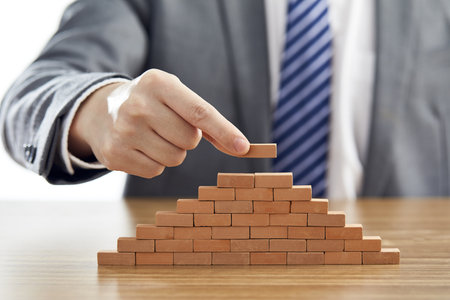 A businessman in a suit putting the last piece of a pyramid using wooden blocks - success conceptの写真素材