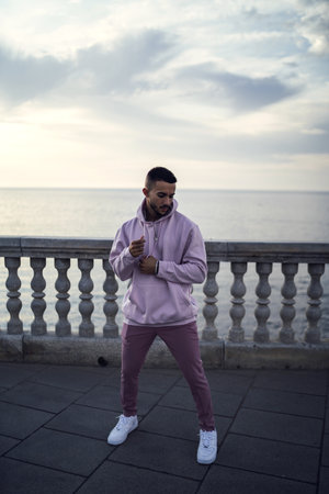 A vertical shot of a young attractive male in a pink street style outfit posing near the seaの写真素材