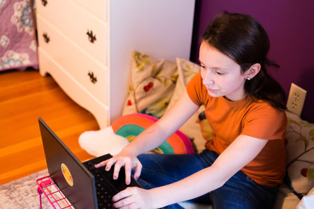 Young girl using laptop. Homeschooling, hand on keyboard in bedroom.