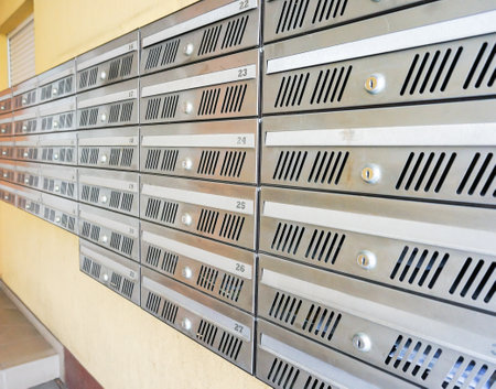 A closeup of silver mailboxes on the yellow wall in the buildingの写真素材