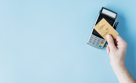 Contactless payment, paypass. Hand hold bank card near terminal on Blue background copy space.