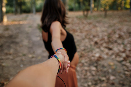 A closeup of a pregnant lady holding her partner's hand and posing for the camera in a parkの写真素材