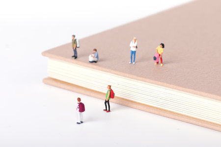 A view of little figurines of students standing on and around a textbook on white backgroundの写真素材