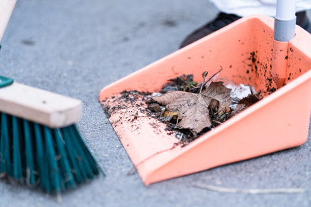 A closeup of a green street broom and dustpan used in cleaning a pavementの写真素材