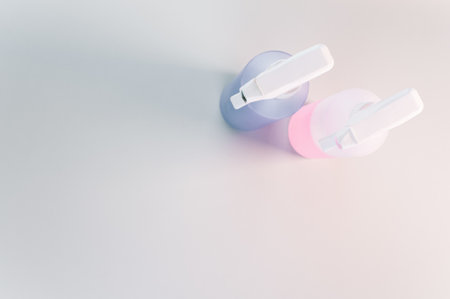 A high angle shot of two spray bottles with pink and purple liquid in them, on a white surface