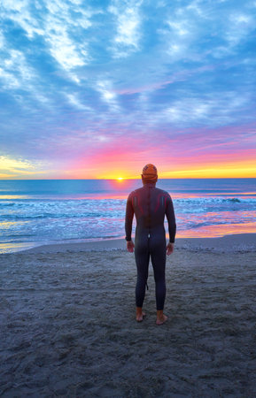 A vertical shot of an athlete swimmer on the beach against a beautiful sunriseの写真素材