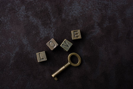 A top view of a metal key and blocks that spell LOVE, on a dark surfaceの写真素材