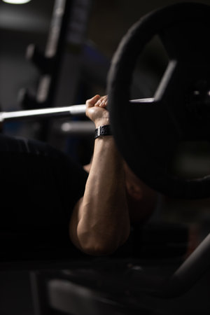 A vertical shot of a person lifting weights in a gym with a dark blurry backgroundの写真素材