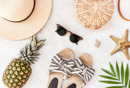 A flat lay shot of sunglasses, a straw hat, a bag, plant leaves, a starfish, a pineapple and sandalsの写真素材