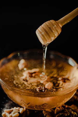 Wooden honey spoon dipped in a jar full of honey and nuts placed on a black background. Honey...