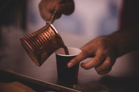 A closeup shot of a male pouring out Turkish coffee into a cupの写真素材
